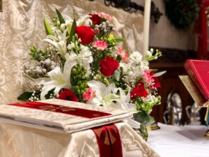 An image of green, white, and red flowers set on our altar at Christmas Eve